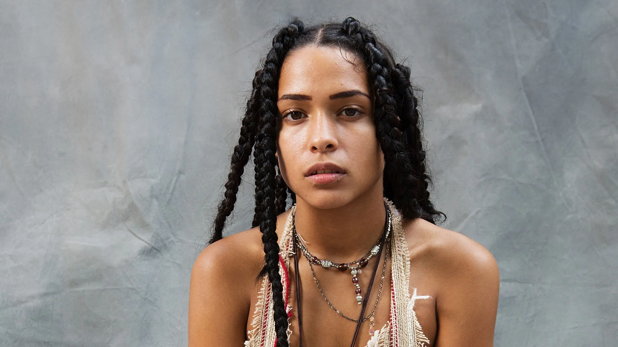 A portrait of an Afro-Indigenous woman with braids and traditional necklaces